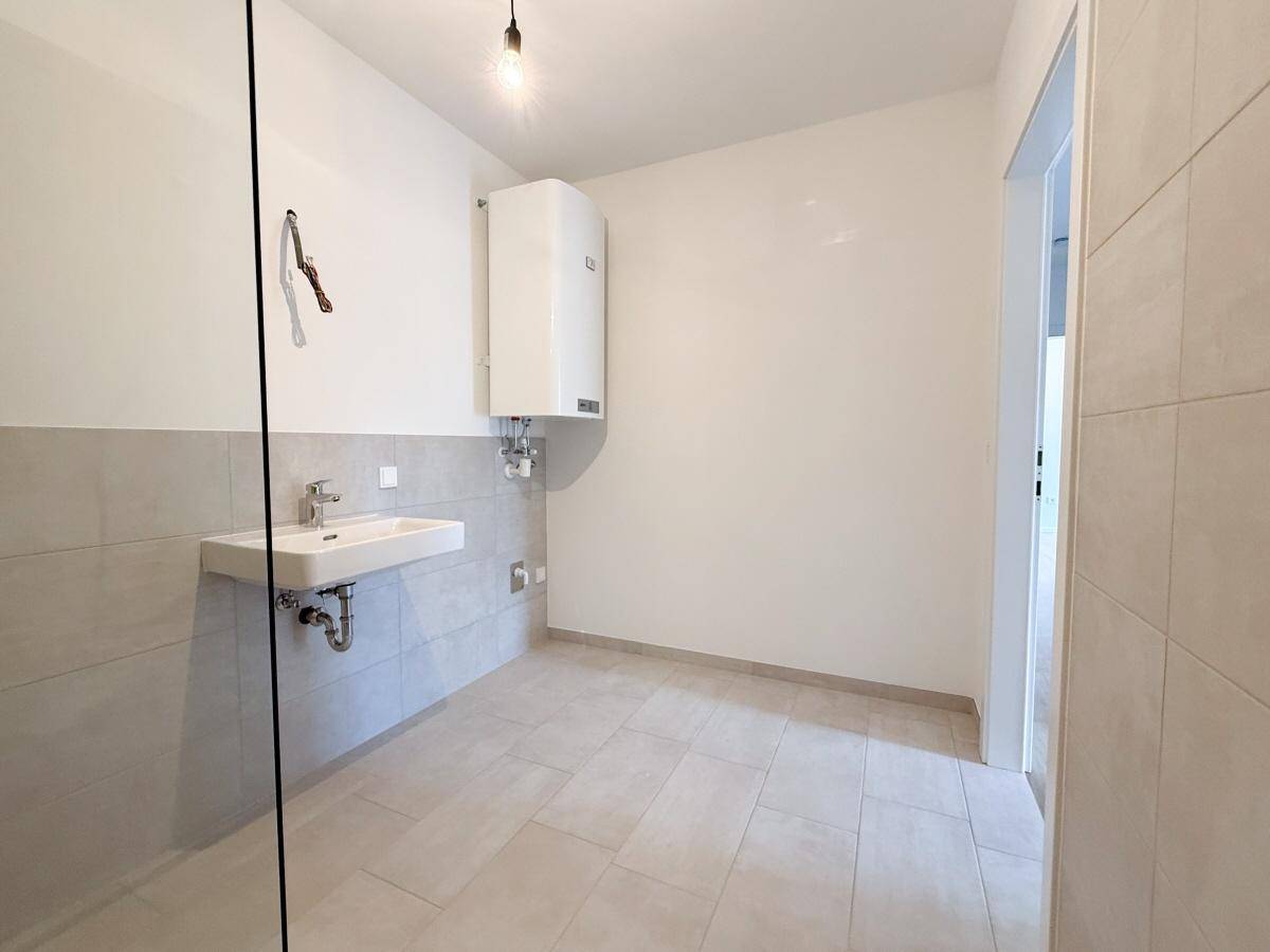 Modernes Badezimmer mit begehbarer Dusche und Waschbecken, halbhoch gefliest in hellen Tönen.