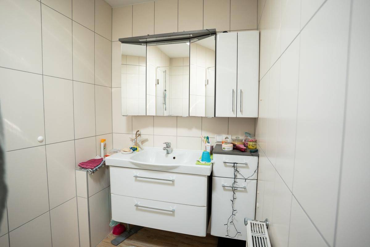 Modernes Badezimmer mit Waschtisch, Spiegelschrank und hellen Fliesen an den Wänden.