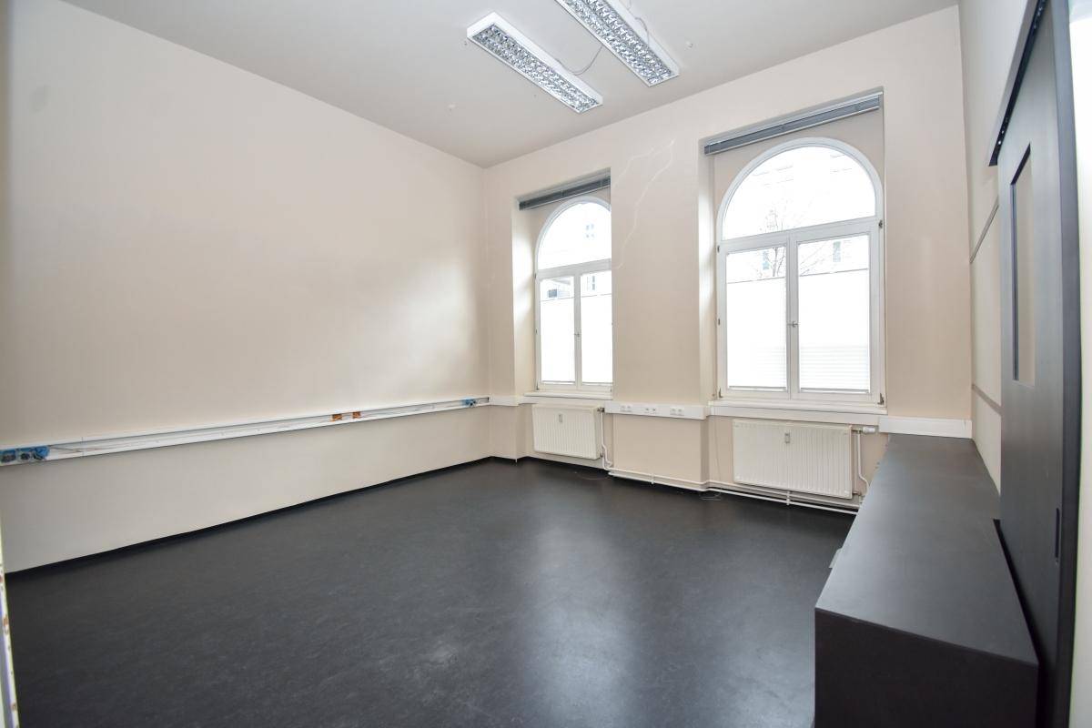 Geräumiger Büroraum mit hohen Decken, großen Bogenfenstern und dunklem Vinylboden, bietet viel Platz.