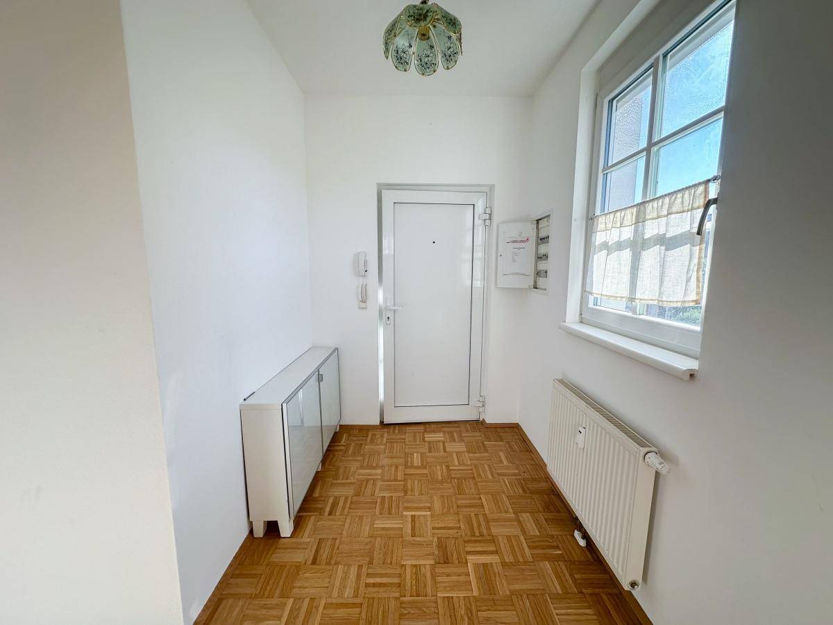 Heller Eingangsbereich mit Parkettboden, Fenster und einem kleinen Schrank.