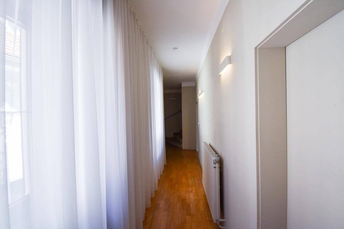 Heller Flur mit Holzfußboden, weißen Wänden und langen, transparenten Vorhängen entlang der Fensterfront.