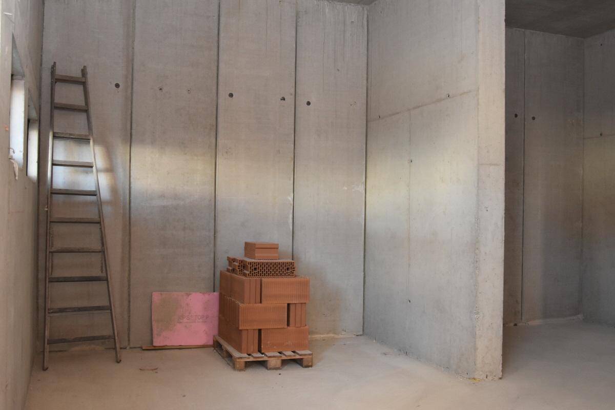 Rohbau eines Gewerberaums mit hohen Betonwänden, einer Leiter und Baustoffen am Boden.
