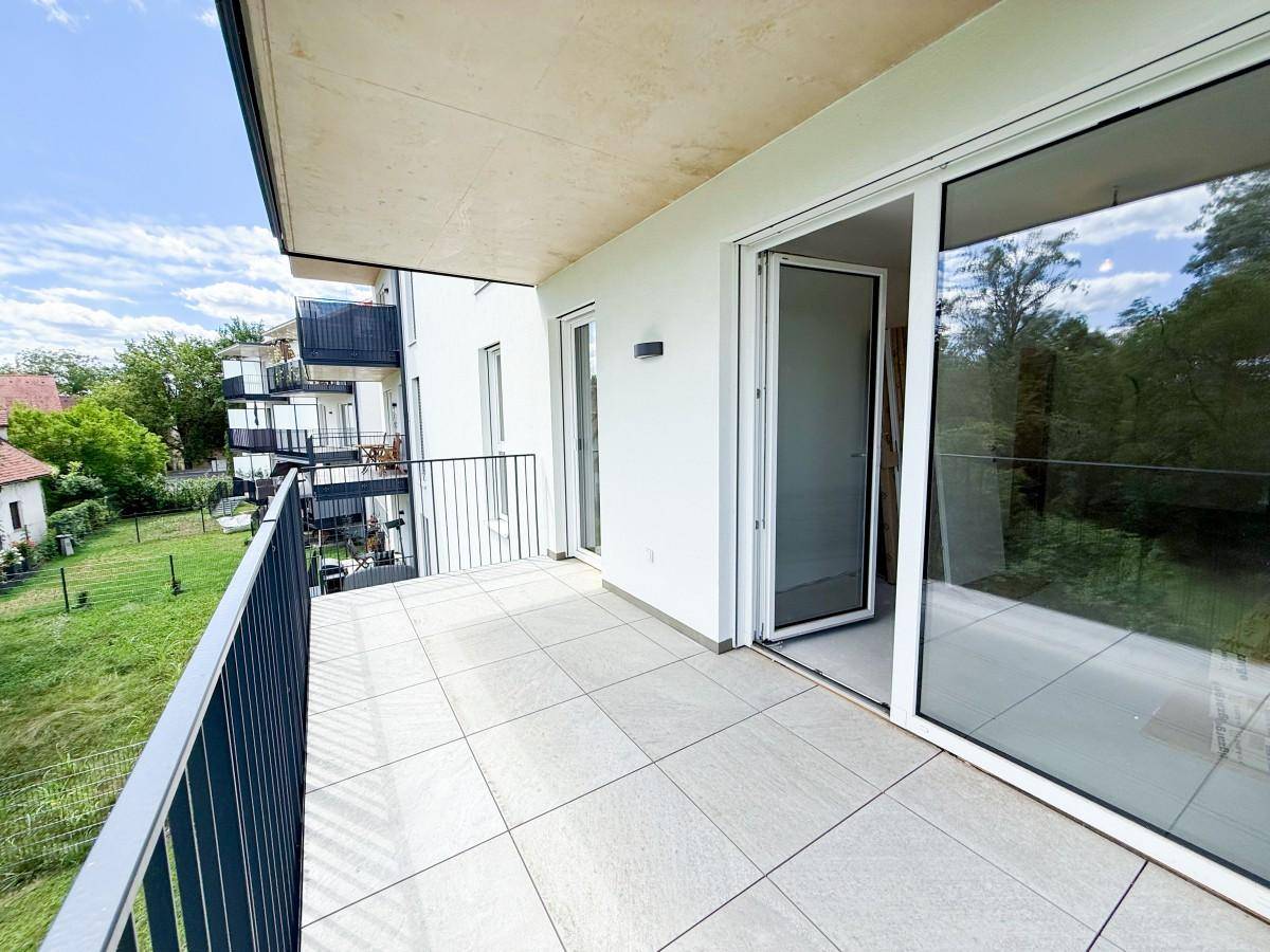 Moderner Balkon mit Fliesenboden und Schiebetür, bietet einen weiten Blick auf die Umgebung und Natur.