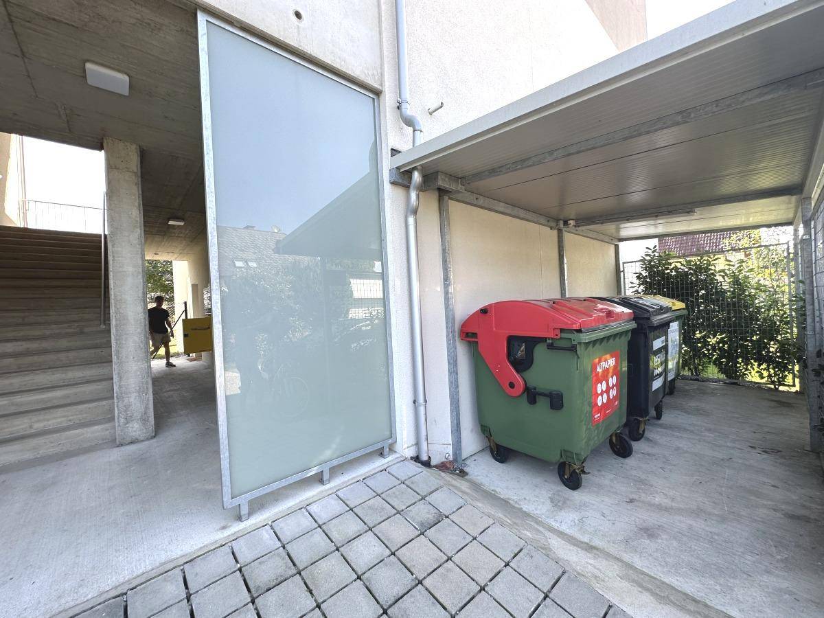 Eingangsbereich des Gebäudes mit Treppenhaus und überdachtem Bereich für Mülltonnen.