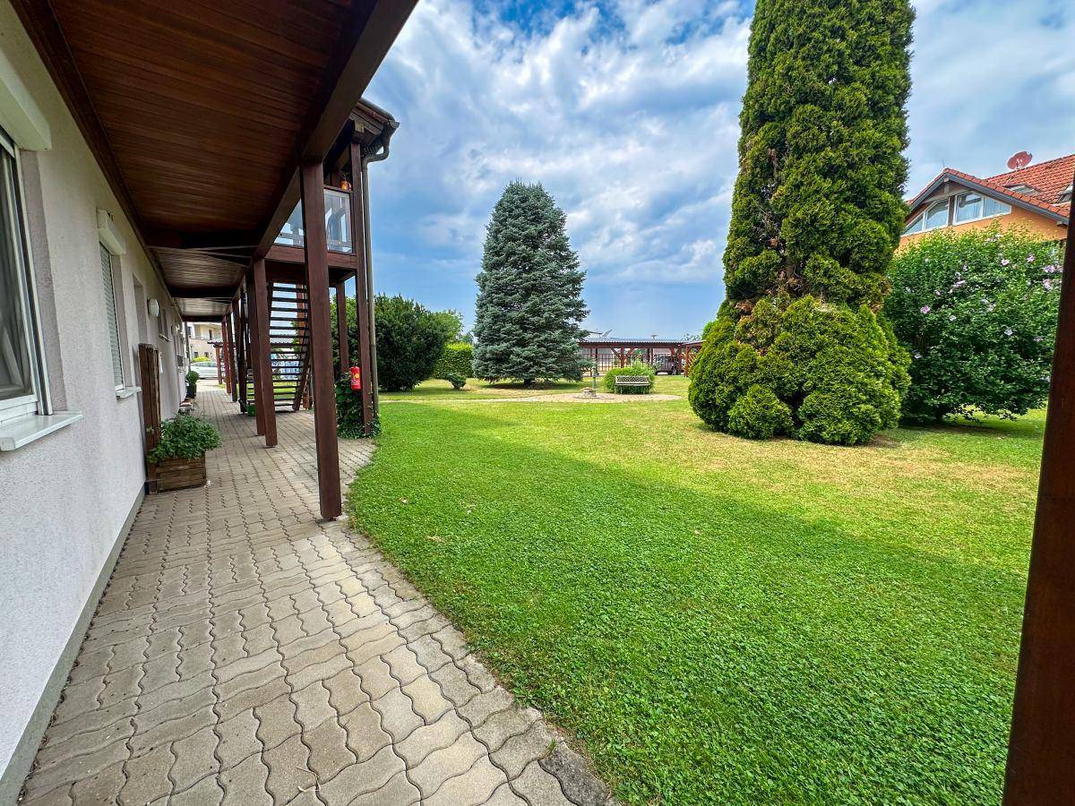 Gepflegter Gartenweg entlang des Hauses mit weitläufiger Rasenfläche und hohen Bäumen.