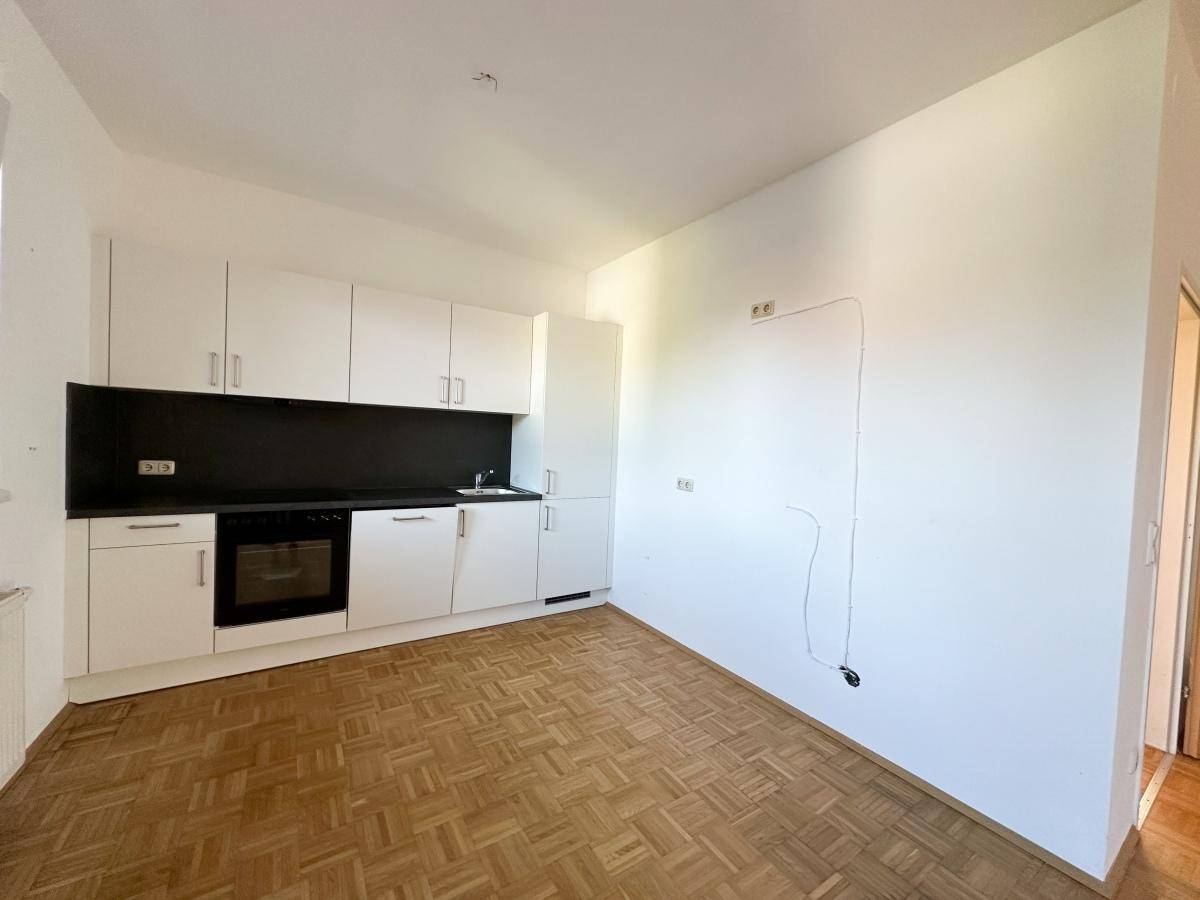 Moderne Küchenzeile mit weißen Schränken, schwarzer Arbeitsplatte und integriertem Backofen.