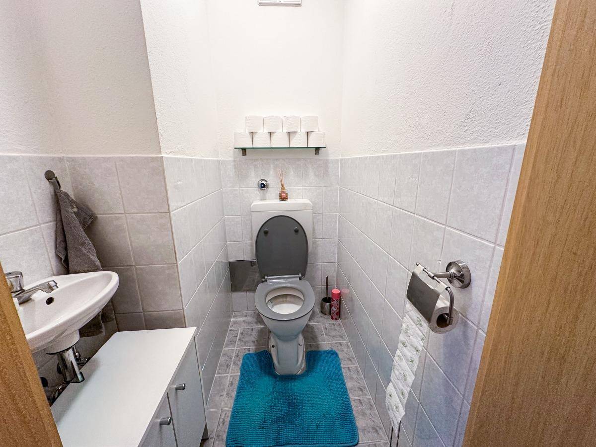 Kleines Gäste-WC mit Toilette, Waschbecken und hellen Wandfliesen.