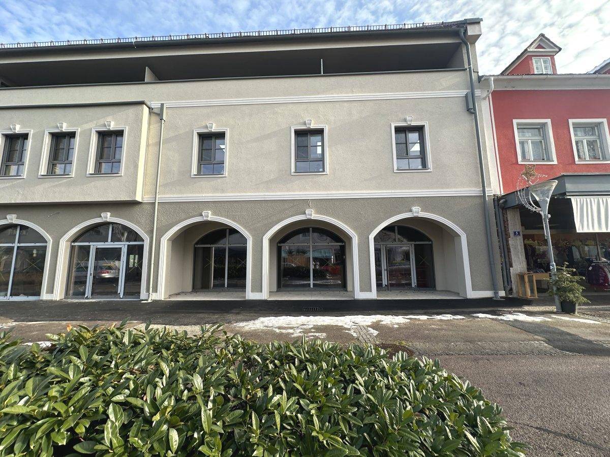 Fassade eines modernen Gebäudes mit eleganten Bogenfenstern im Erdgeschoss und gepflegter Putzfassade.