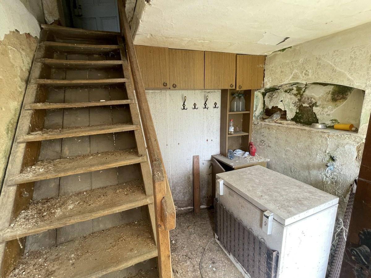 Eingangsbereich mit alter Holztreppe, Schränken und einem Gefrierschrank in schlechtem Zustand.