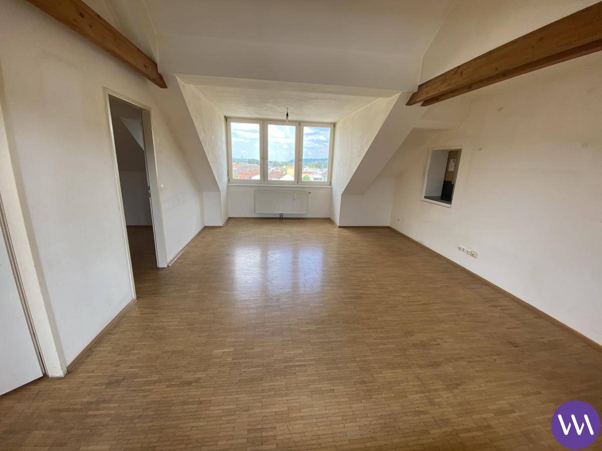 Geräumiges Wohnzimmer im Dachgeschoss mit Holzbalken, Parkettboden und weitem Ausblick.