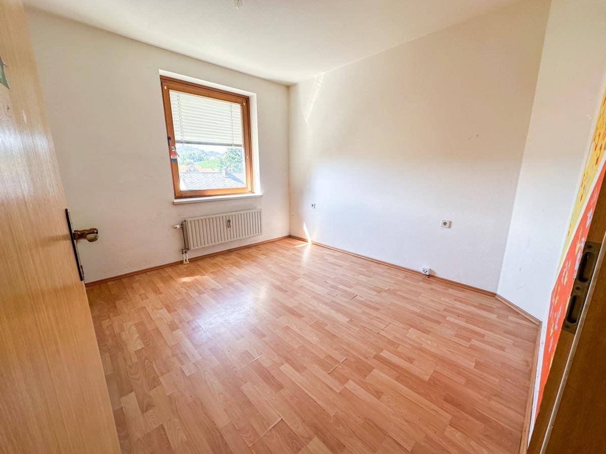 Helles Zimmer mit Laminatboden und Fenster mit Jalousien, ideal als Schlaf- oder Arbeitszimmer.