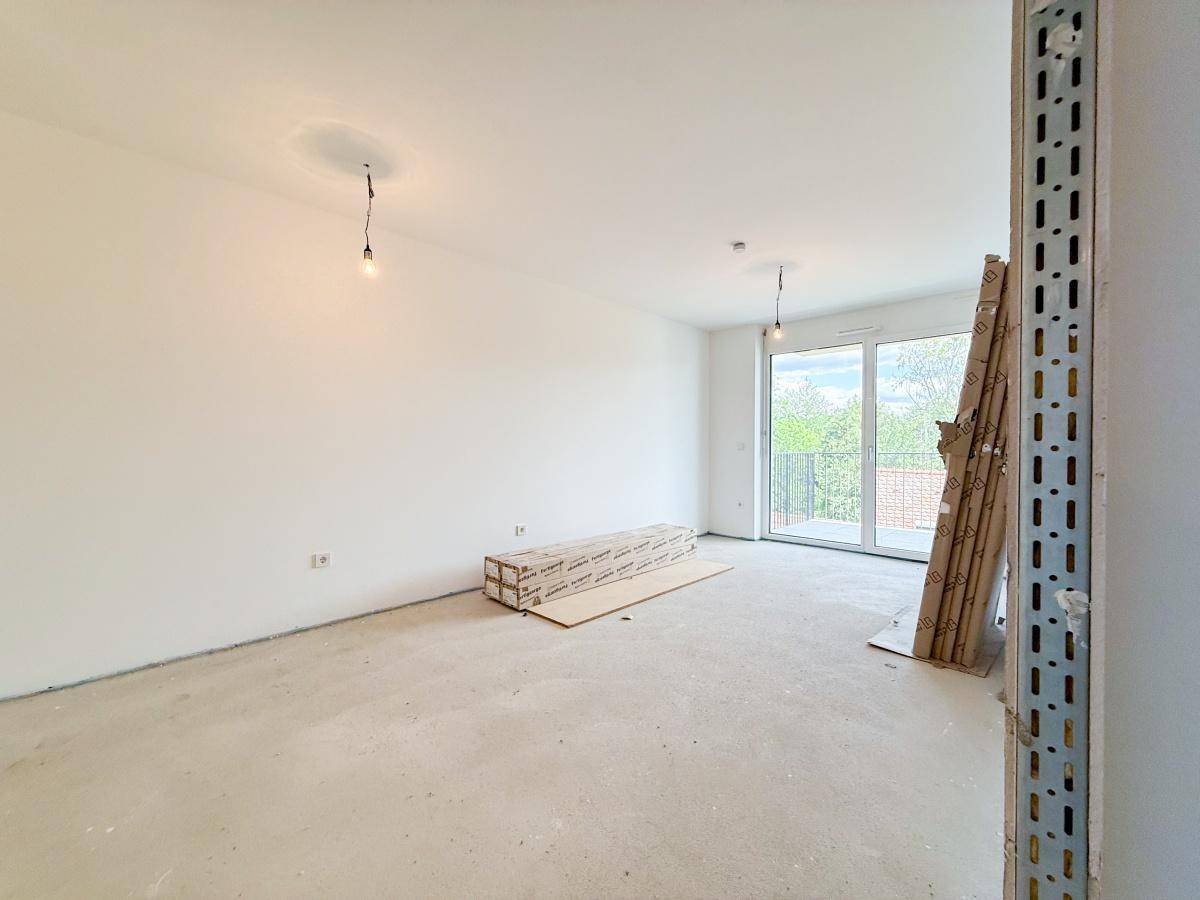 Großer Wohnbereich im Rohbau mit Schiebetür zum Balkon und viel Potenzial.