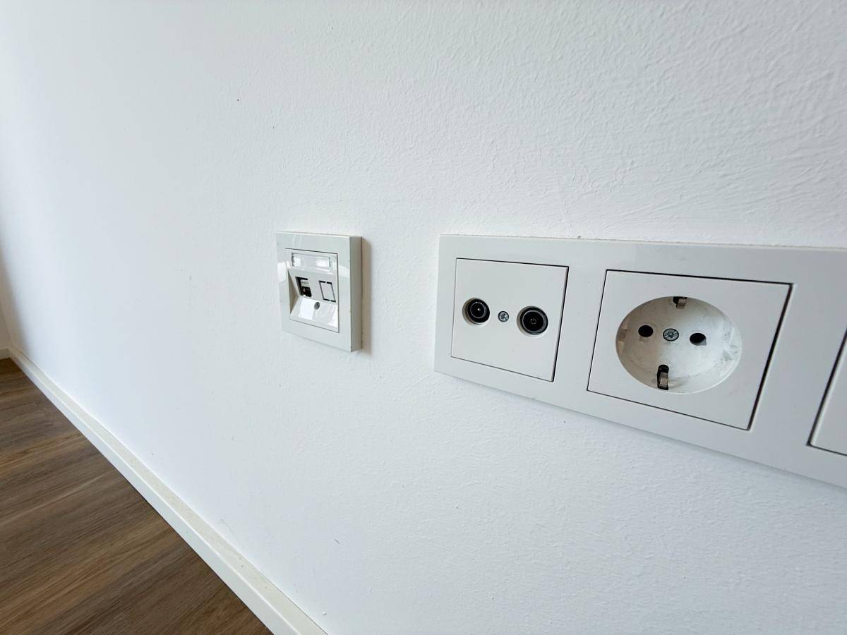 Weiße Wand mit modernen Steckdosen für Strom, TV und Netzwerkanschluss.