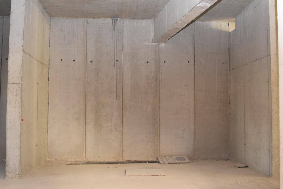 Rohbau eines Raumes mit hohen Betonwänden und einem sichtbaren Betonbalken an der Decke.