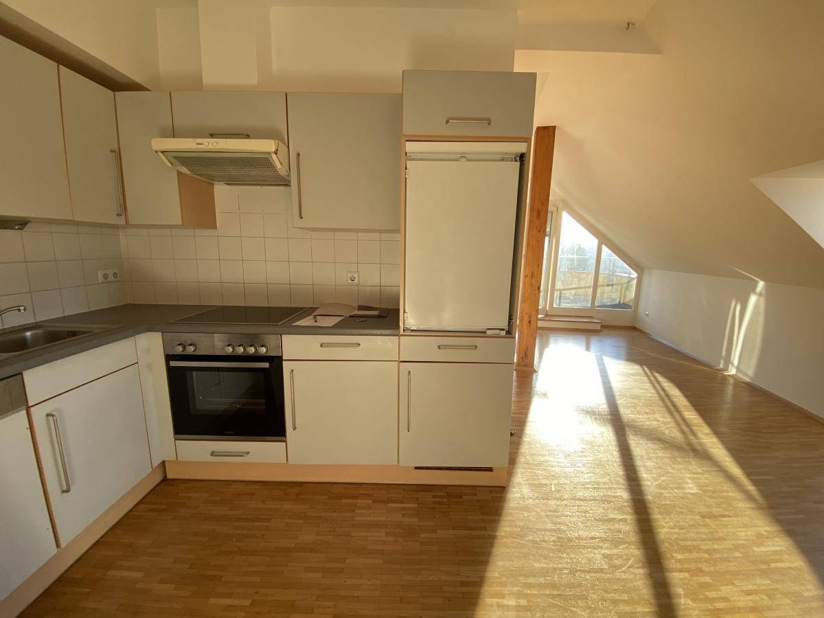 Funktionale Küche mit hellgrauen Schränken, integrierten Geräten und Holzboden im Dachgeschoss.