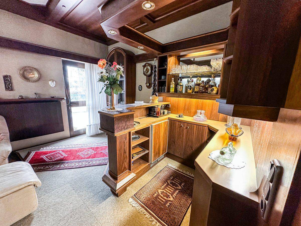 Wohnzimmer mit eingebauter Bar, Teppichboden und Holzvertäfelung an Decke und Wänden.
