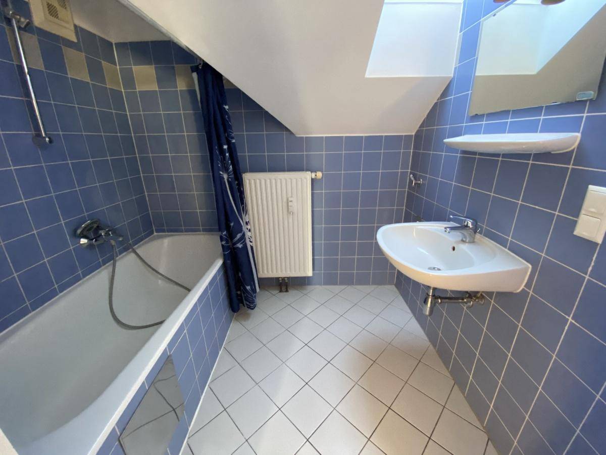 Badezimmer mit blauen Wandfliesen, Badewanne, Waschbecken und einem Dachfenster für natürliches Licht.