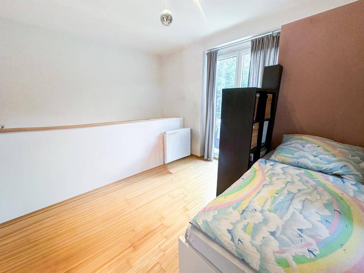Kinderzimmer mit Holzboden, Fenster und einem Bett mit bunter Bettwäsche.