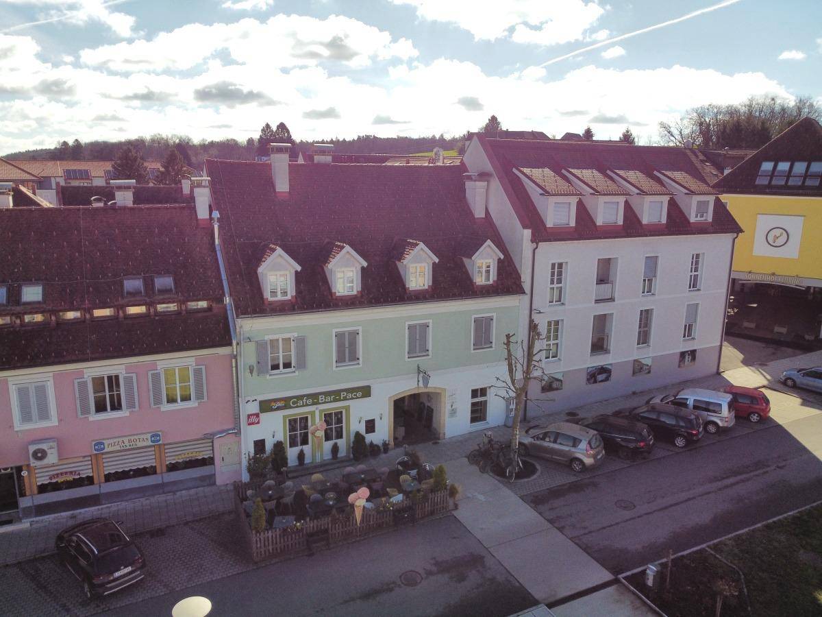 Luftaufnahme des Gebäudes mit Café im Erdgeschoss und umliegender Bebauung unter bewölktem Himmel.