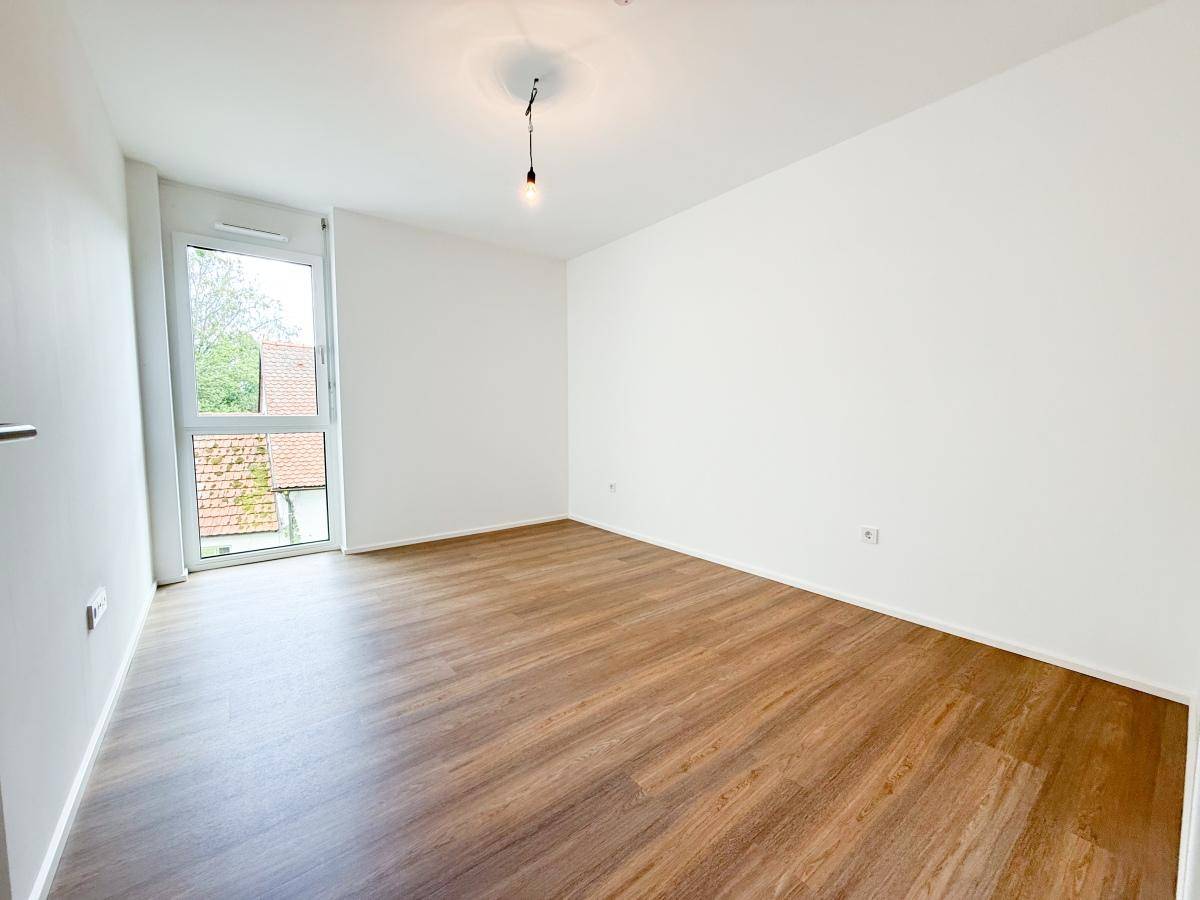 Helles Schlafzimmer mit Laminatboden und großem Fenster, bietet viel Tageslicht und Ausblick.