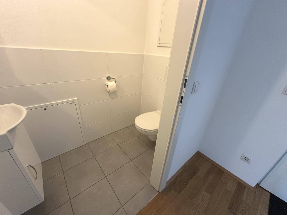 Separates Gäste-WC mit Toilette, kleinem Waschbecken und hellen Fliesen.