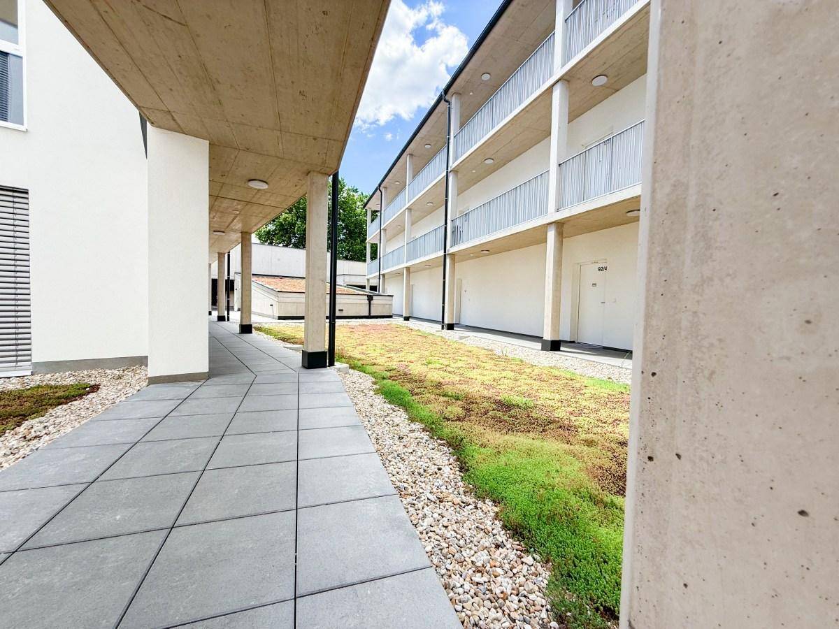 Ansicht eines modernen Wohngebäudes mit begrüntem Innenhof und Zugangswegen.