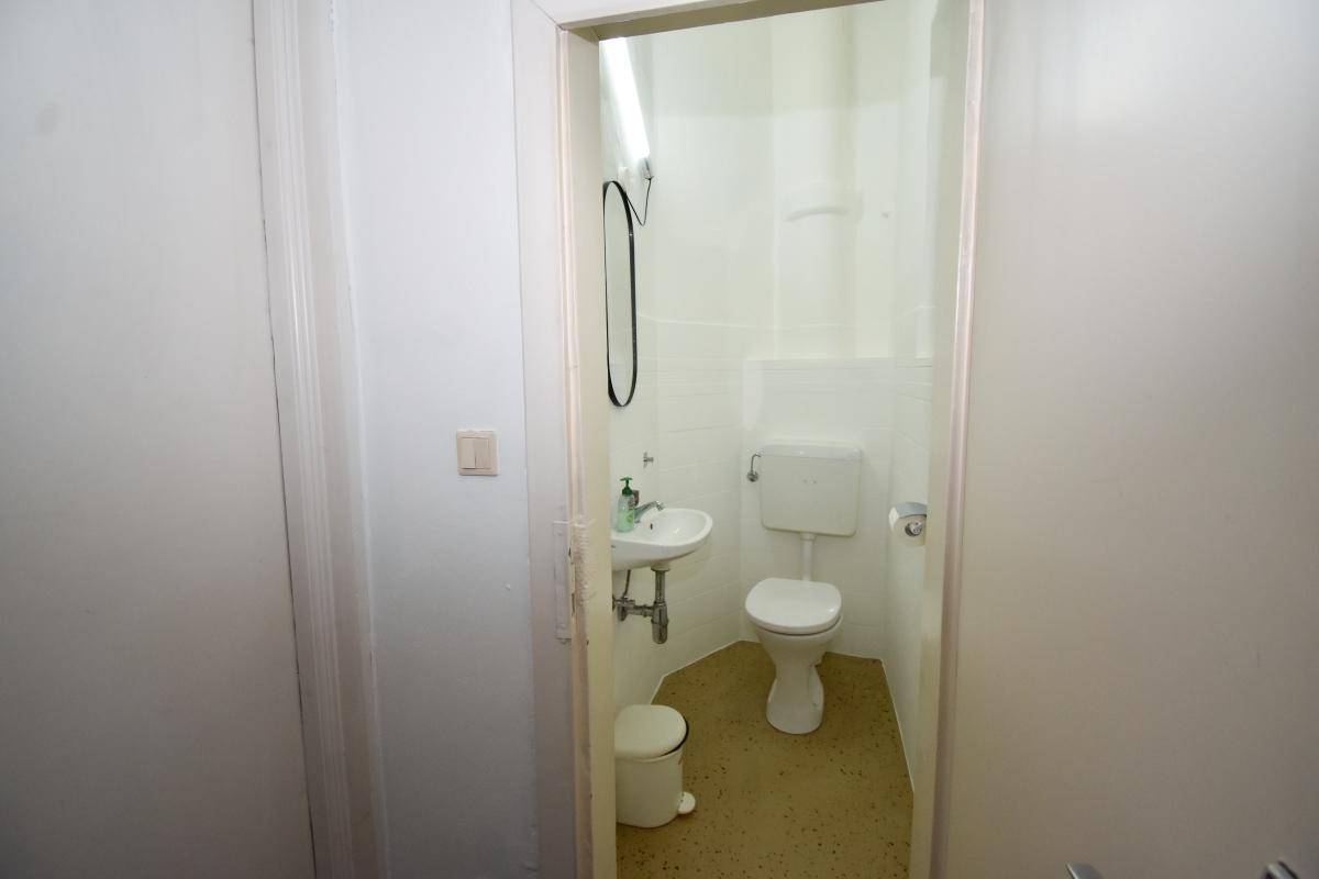 Kleine, einfache Toilette mit Waschbecken und hellem Fliesenboden, funktional und sauber.
