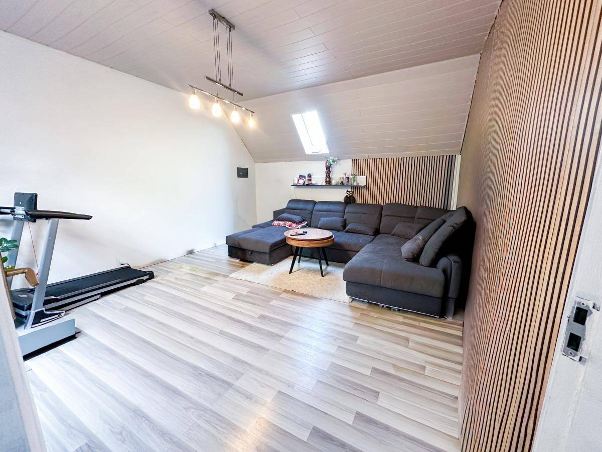 Geräumiges Wohnzimmer mit großem Ecksofa, Holzwandverkleidung und Dachfenster.
