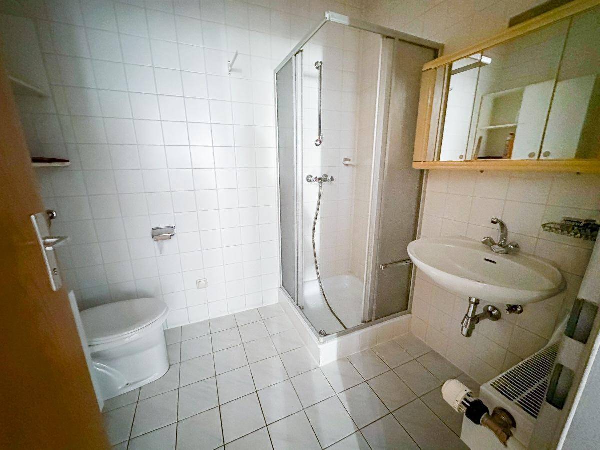 Helles Badezimmer mit weißen Fliesen, Duschkabine und Waschbecken mit Spiegelschrank.