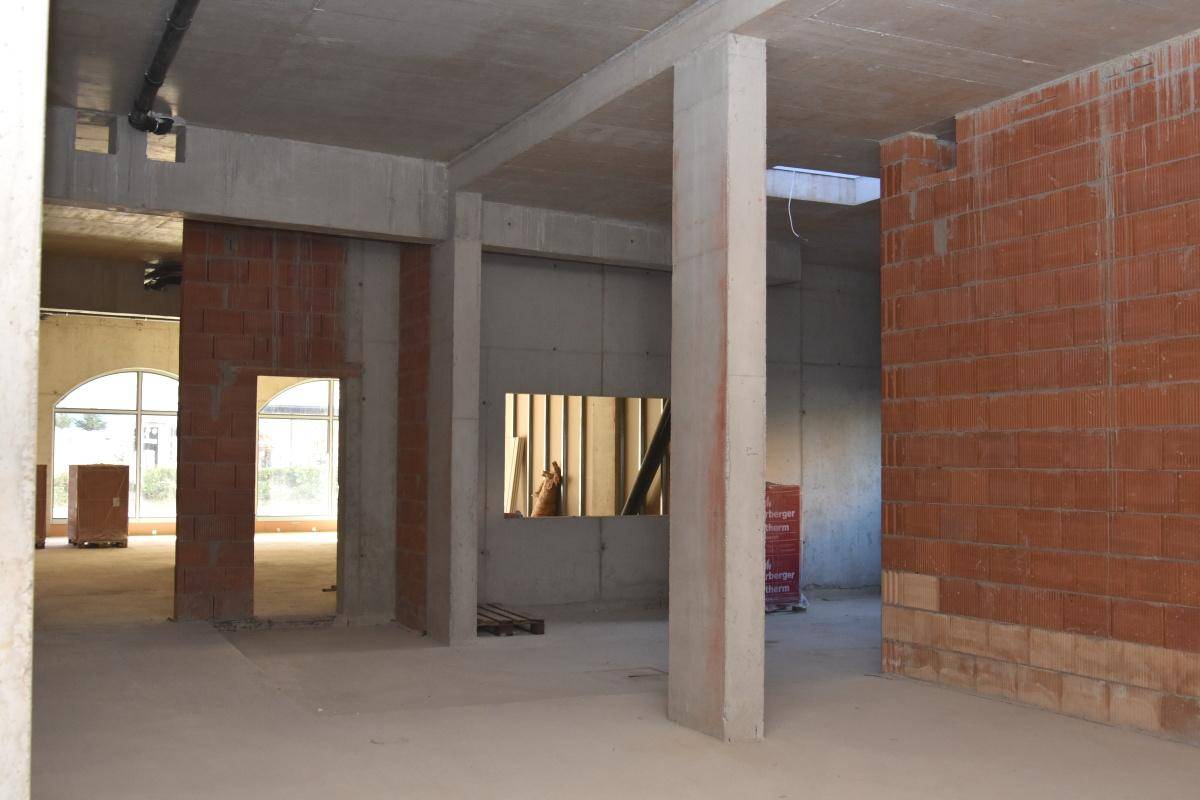 Rohbau eines Gewerberaums mit Betonstützen, Ziegelwänden und einer hohen Betondecke.