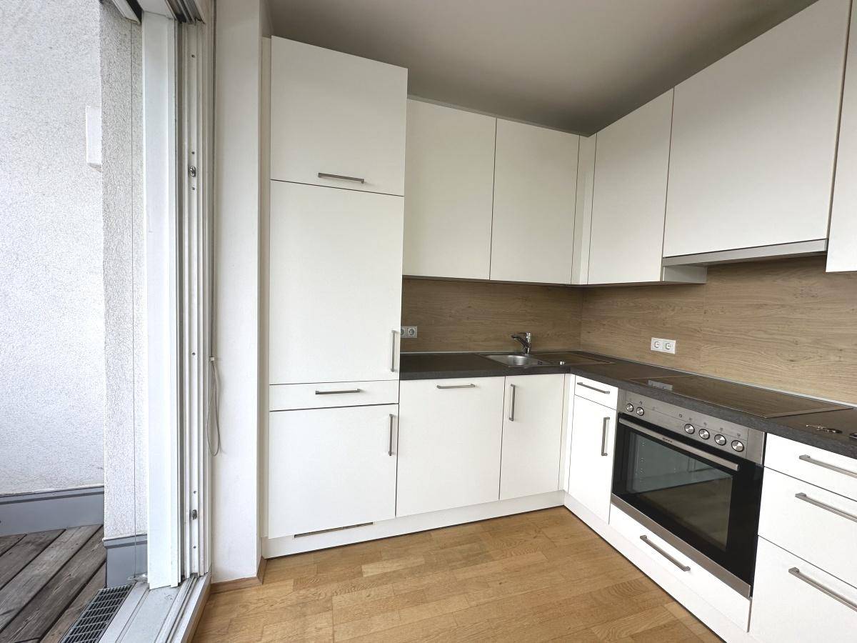 Moderne Einbauküche mit weißen Schränken, integrierten Geräten und Zugang zum Balkon.
