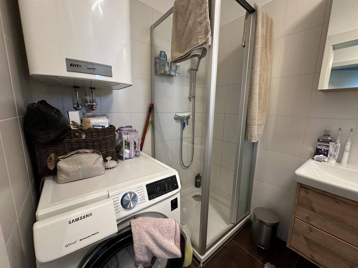 Modernes Badezimmer mit Duschkabine und Waschmaschine, praktisch und funktional ausgestattet.