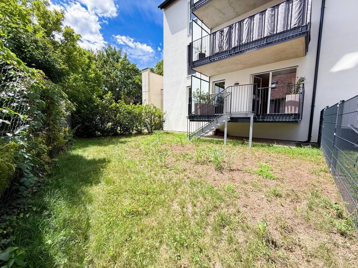 Gepflegter Gartenbereich mit Rasenfläche und Hecke, angrenzend an das moderne Wohngebäude.
