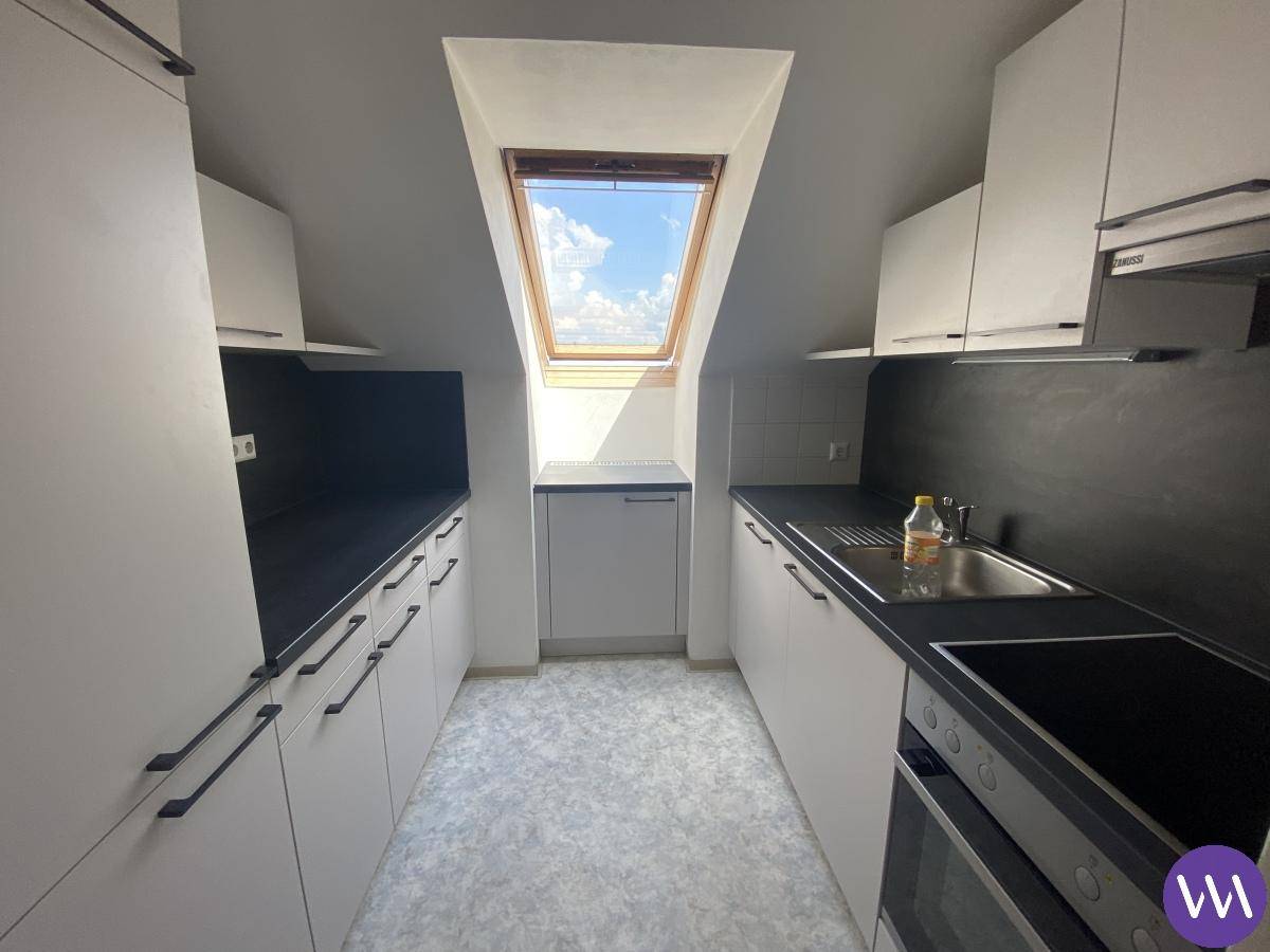 Moderne Küche im Dachgeschoss mit Dachfenster, weißen Schränken und dunkler Arbeitsplatte.