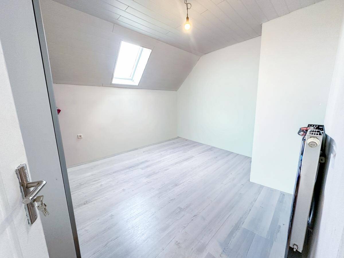 Helles Zimmer mit Dachschräge, Laminatboden und einem Dachfenster für viel Tageslicht.