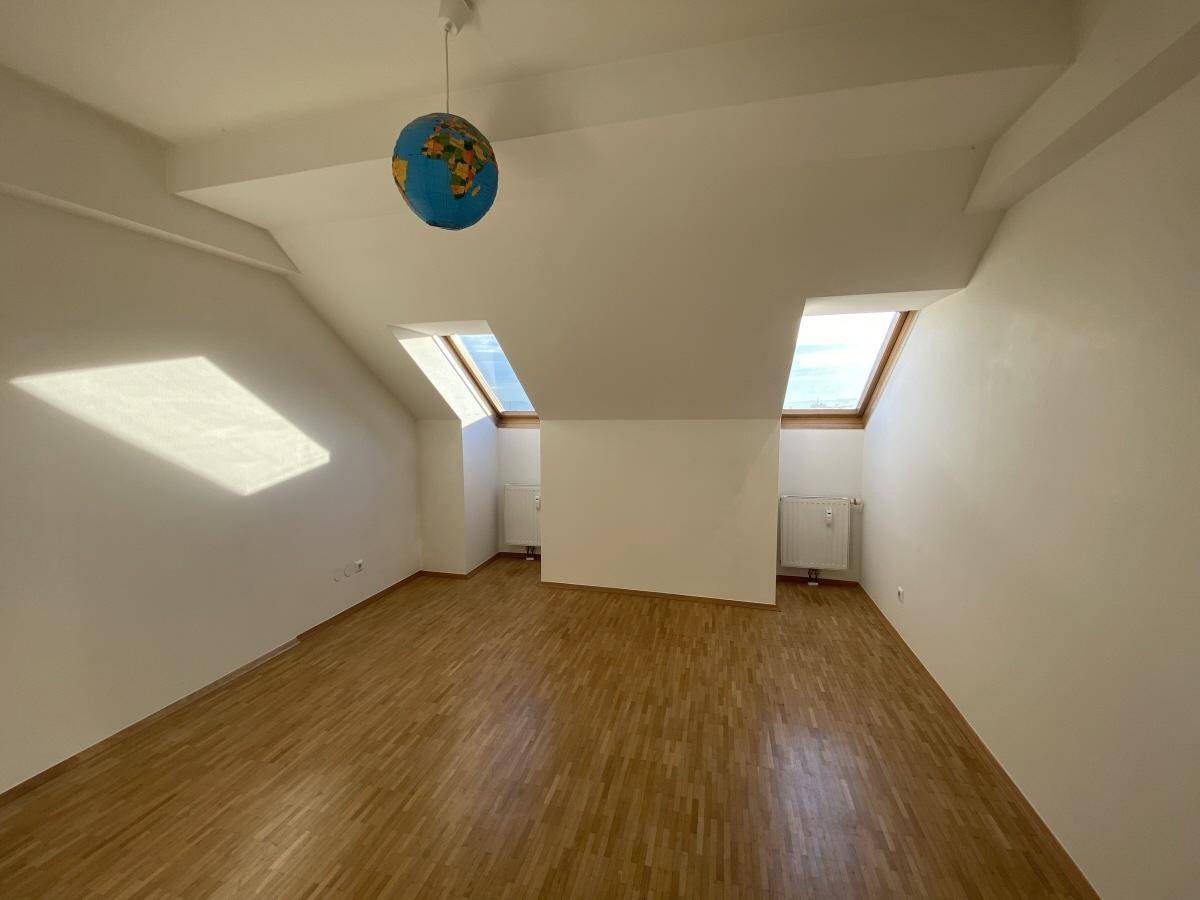 Freundliches Dachgeschosszimmer mit Holzboden, Dachfenstern und einer dekorativen Globuslampe.