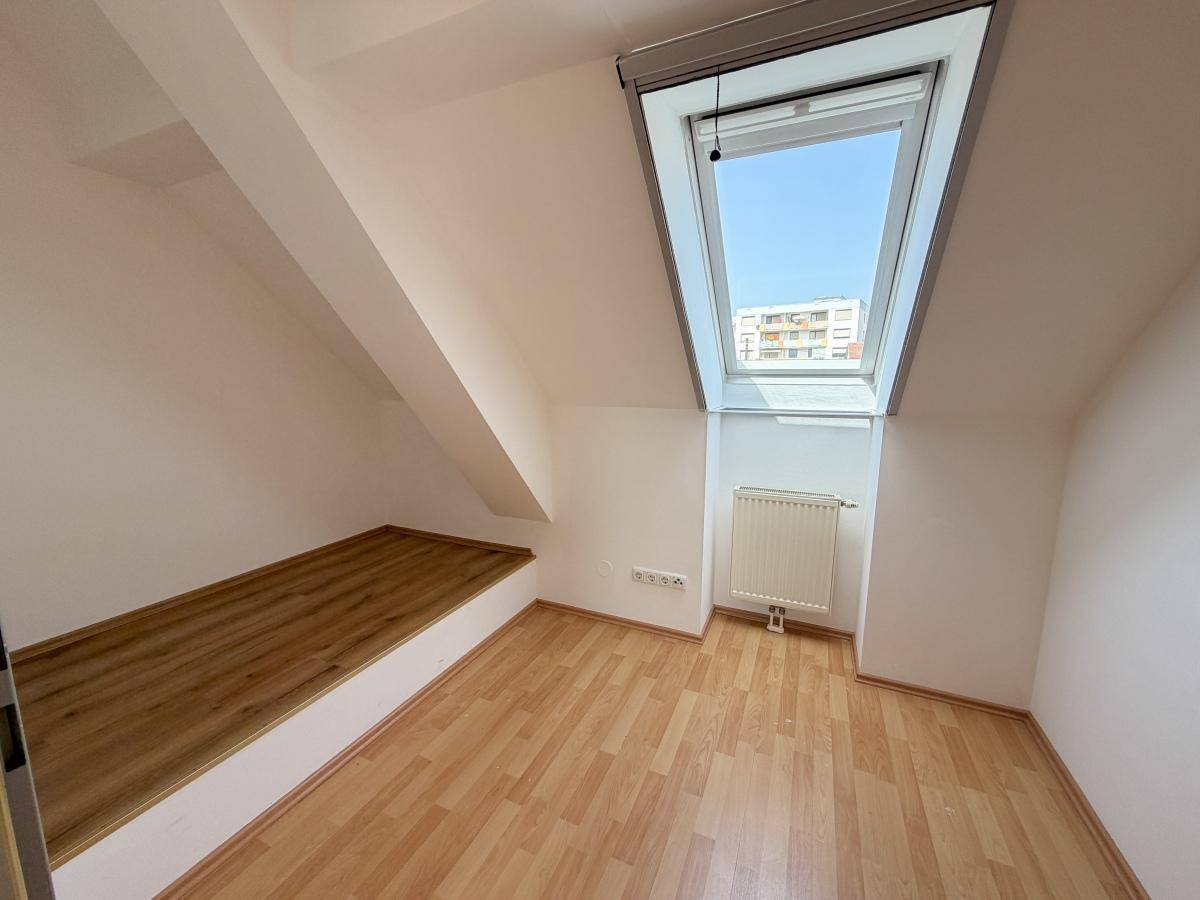 Helles Dachzimmer mit Dachfenster, Heizkörper und einer praktischen Holzablage unter der Schräge.