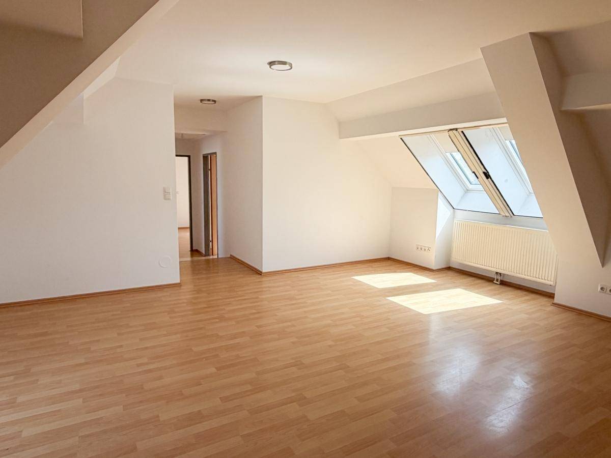 Heller und geräumiger Wohnbereich im Dachgeschoss mit Laminatboden, Dachfenster und Heizkörper.