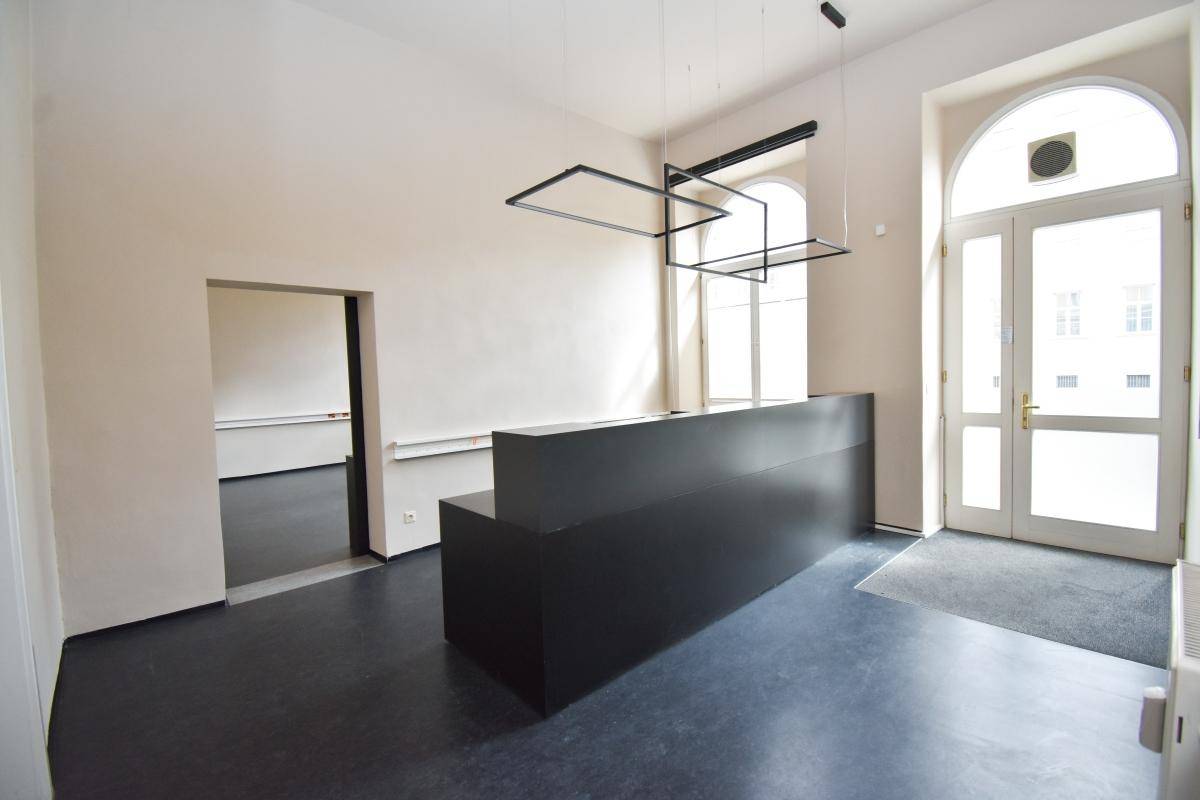 Empfangsbereich mit einer schwarzen Theke, hohen Decken und einer großen Eingangstür mit Bogenfenster.