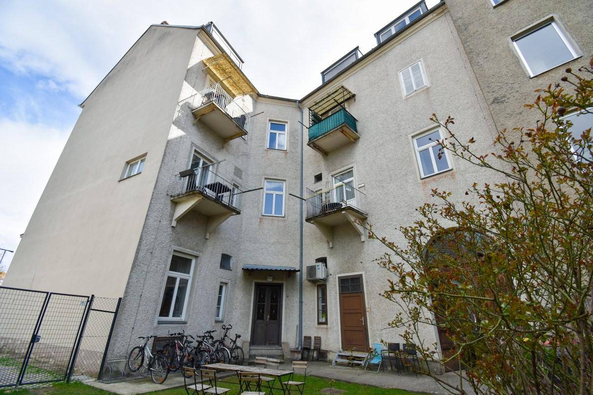 Hinterhofansicht eines Gebäudes mit mehreren Balkonen und einem kleinen begrünten Innenhof.