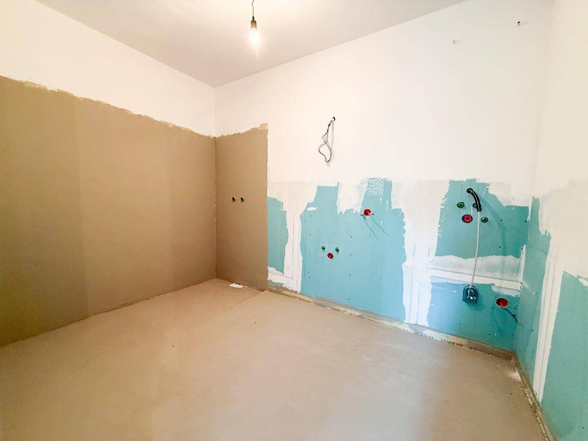 Badezimmer im Rohbau mit vorbereiteten Anschlüssen für Dusche und Waschbecken.