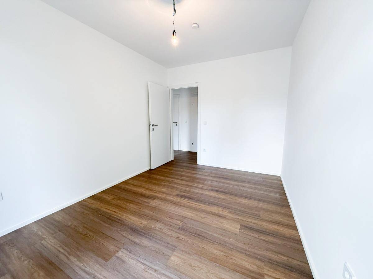 Schlafzimmer mit Laminatboden und weiß gestrichenen Wänden, bietet Zugang zu weiteren Räumen.