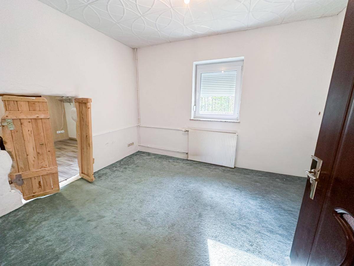 Leeres Zimmer mit grünem Teppichboden und rustikalem Holztürrahmen.
