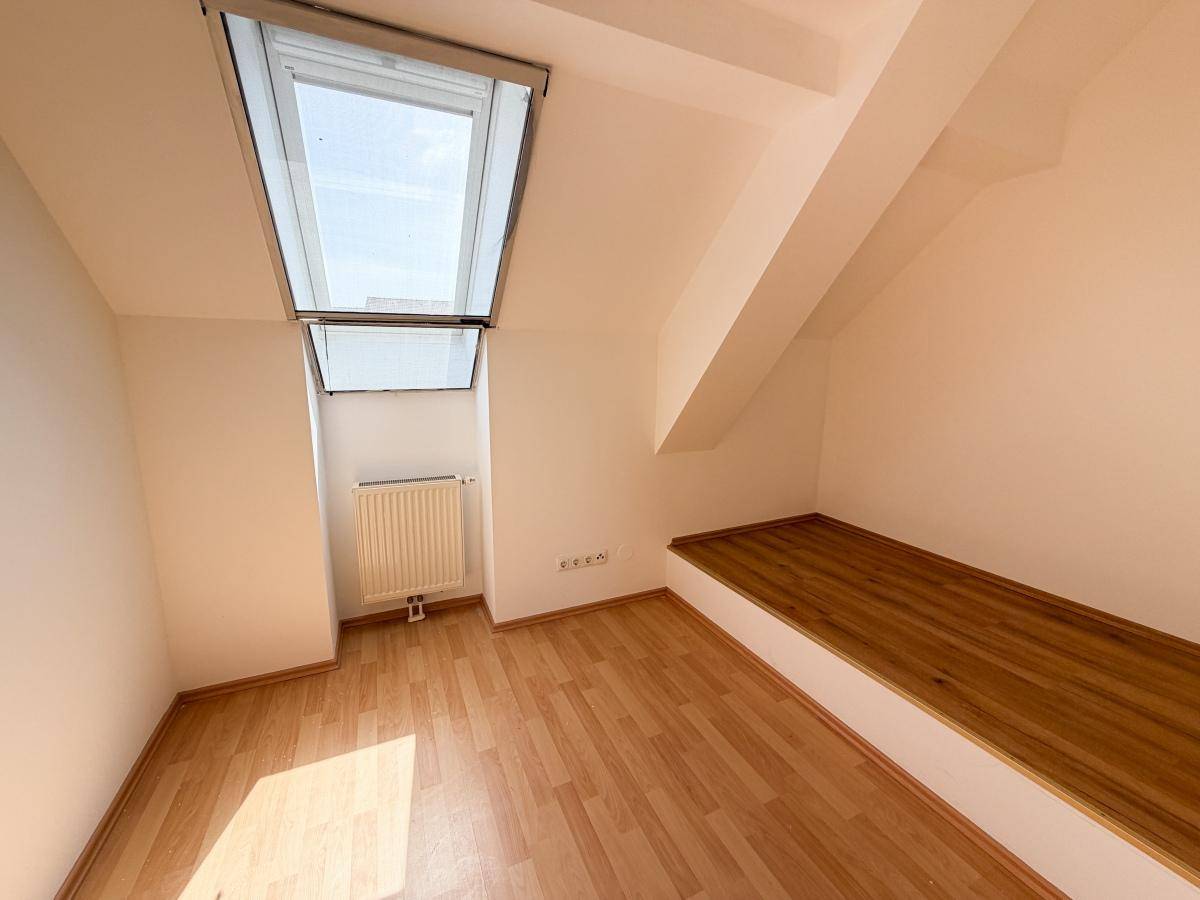 Gemütliches Dachzimmer mit Dachfenster, Heizkörper und einer praktischen Holzablage unter der Schräge.