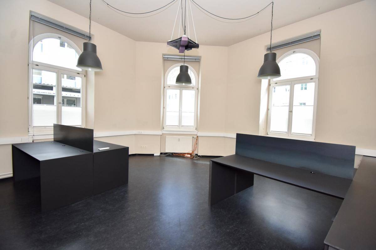 Großer Büroraum mit mehreren Arbeitsplätzen, hohen Decken und großen Fenstern, ausgestattet mit modernen Leuchten.