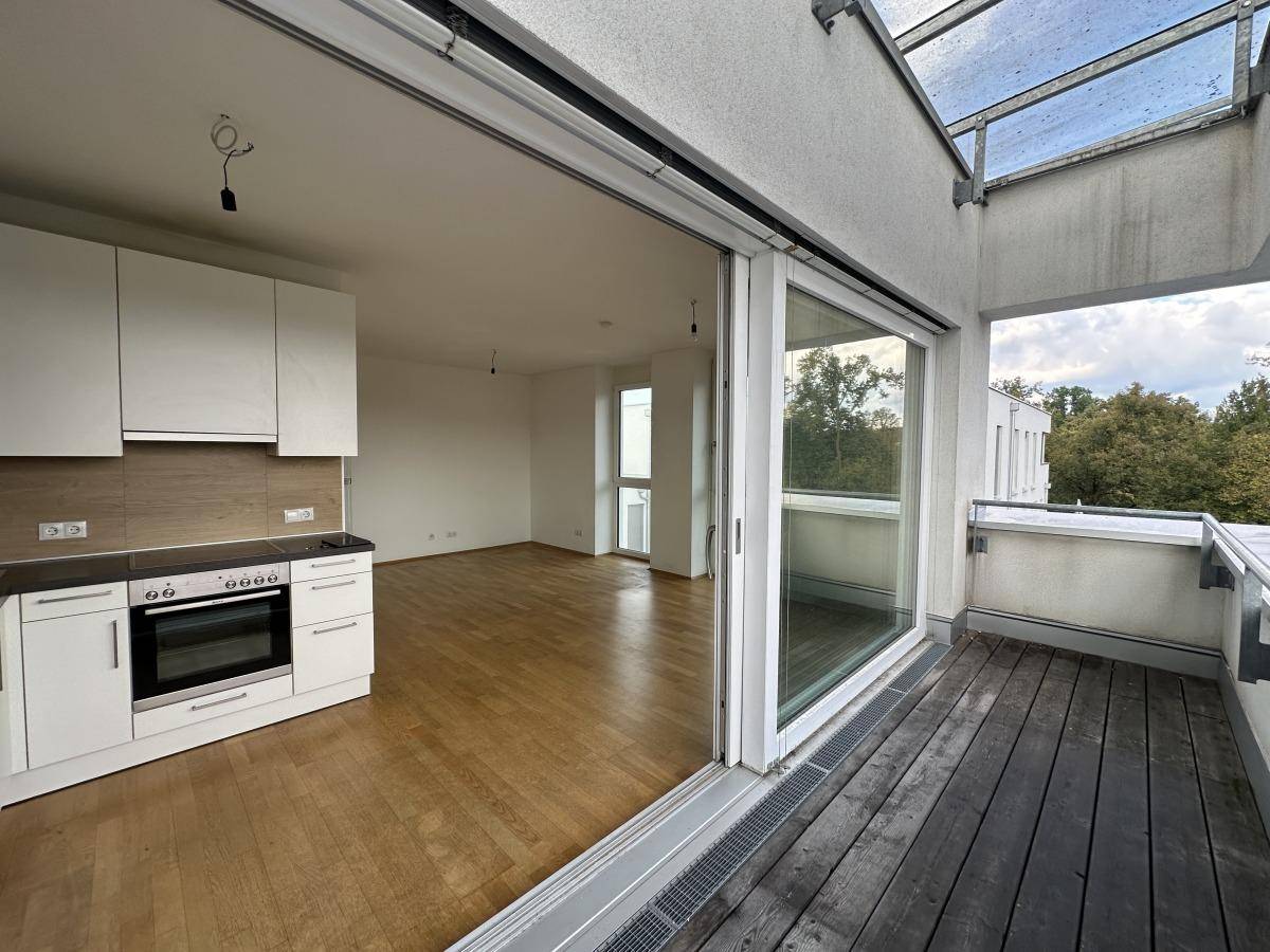 Geräumiger Balkon mit Holzboden und Blick in den offenen Wohnbereich mit Küchenzeile.