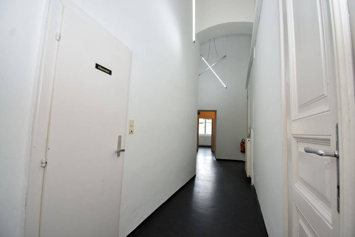 Langer, heller Flur mit weißen Wänden, dunklem Boden und modernen Hängelampen, führt zu verschiedenen Räumen.