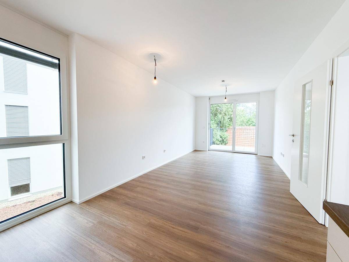 Heller Wohnbereich mit großen Fenstern, Laminatboden und Zugang zum Balkon.