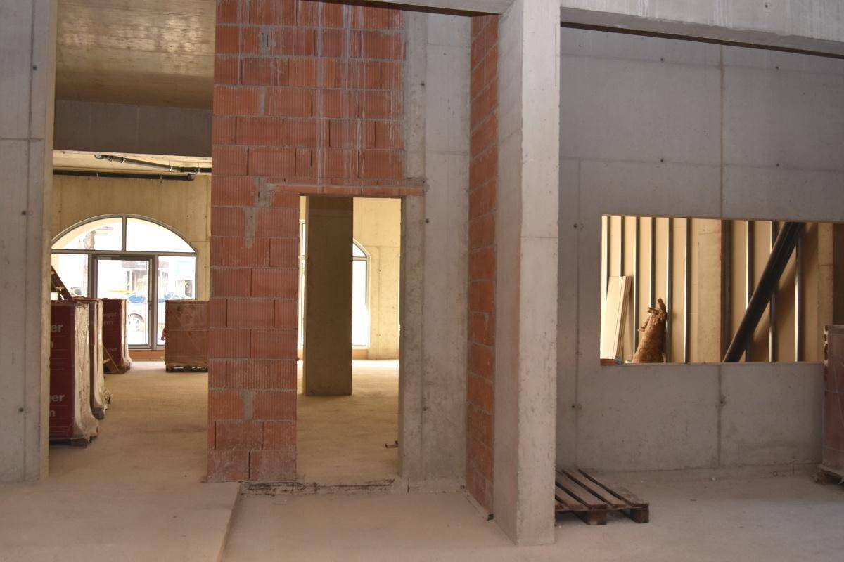 Rohbau mit Beton- und Ziegelwänden, Säulen und Blick in angrenzende Räume mit Bogenfenstern.