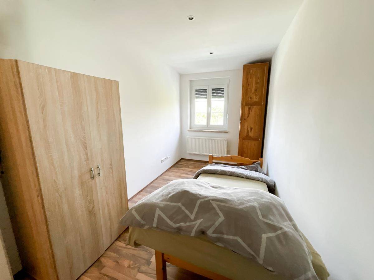Gemütliches Schlafzimmer mit Einzelbett, Holzschrank und Fenster mit Rollladen.
